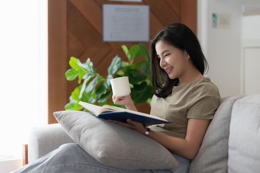 Image of Young Asian woman reading a book sitting on sofa. Lifestyle and Relax concept