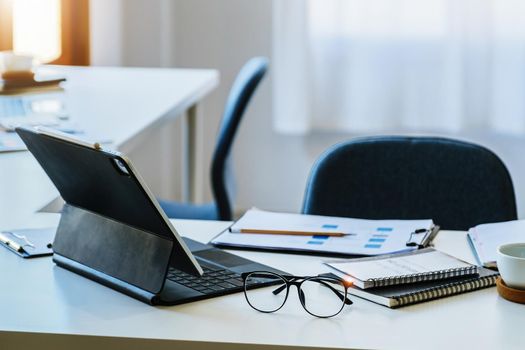 Focus on glasses with coffee mugs, books, documents with tablet computers on the desk.