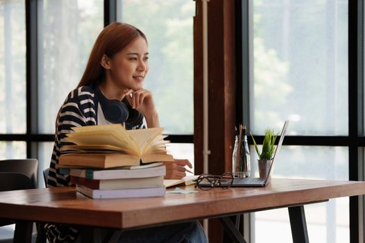 Young asian girl student wear headphone and writing a notebook and watching online class by laptop. e-learning education concept