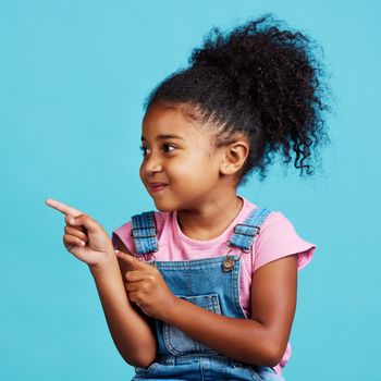 Shot of an adorable little girl pointing at something while standing against a blue background.