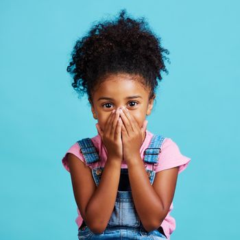 Shot of a little girl looking surprised while posing against a blue background.