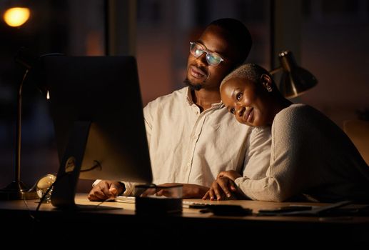 Shot of two affectionate businesspeople working together on a computer in an office at night.