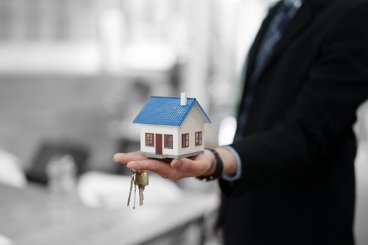 Accountant, businessman, real estate agent, Asian business man handing model house and keys to customers along with house interest calculation documents for customers to sign.