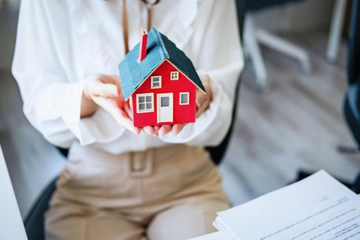 Accountant, businessman, real estate agent, Asian business woman handing model house to customers along with house interest calculation documents for customers to sign