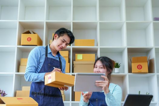 Portrait of a small start-up and SME owner, an Asian male and female entrepreneur checking orders and packing for customers, self-employed, freelance, online selling.