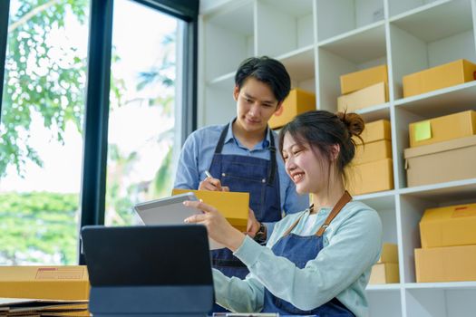 Portrait of a small start-up and SME owner, an Asian male and female entrepreneur checking orders and packing for customers, self-employed, freelance, online selling.