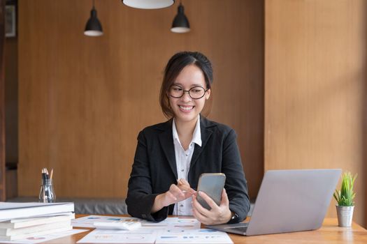 Asian woman holding smart phone while using calculator for business financial accounting calculate money bank loan rent payments manage expenses finances taxes doing paperwork concept, close up