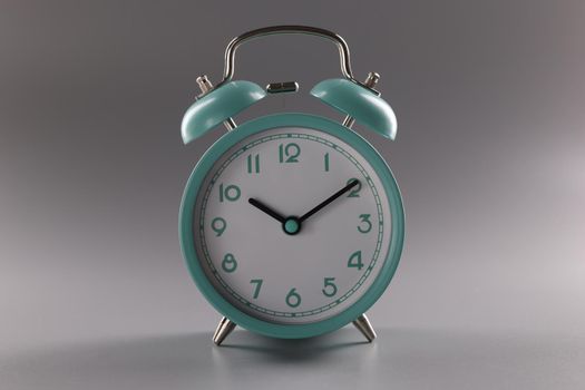 Close-up of single simple designed green retro clock on grey surface. Metal vintage clock on tiny legs stand. Time, timer, alarm, decor, rarity concept