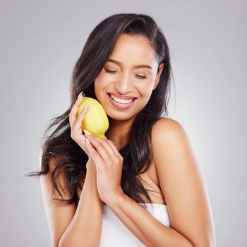 Cropped shot of an attractive young woman posing with a lemon against a grey background.