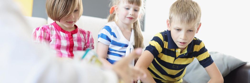 Portrait of kids sitting on sofa and play card game together for development. Brother and sister spend time together on vacation at home. Childhood concept