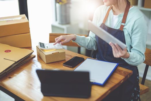 A portrait of .a small start-up and an SME owner, an Asian female entrepreneur using a calculator to calculate profits from selling products online.