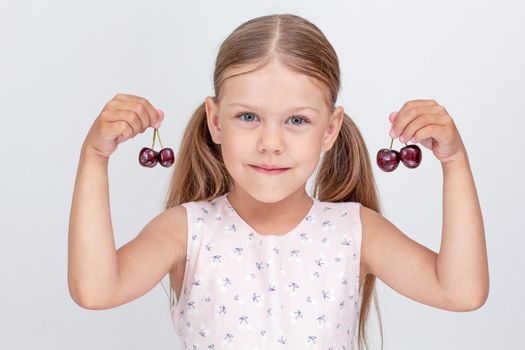 Caucasian little girl of 6 years holding sweet cherry on white background