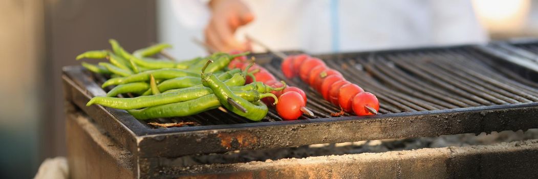 Close-up of amateur chef frying fresh tomatoes and green pepper on grill on open air. Person cooking picnic for friends. Food, cafe, eat, barbeque concept