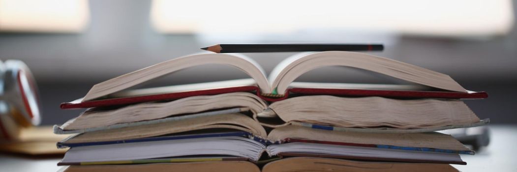 Close-up of stack of books lay on table, undone homework tasks or things to learn at home. Remote education, distance school, knowledge, library concept