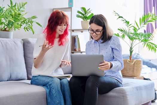 Female teacher teaches student teenage girl, sitting together on couch in office, educational counseling, using laptop. Education, knowledge, individual training, adolescence concept