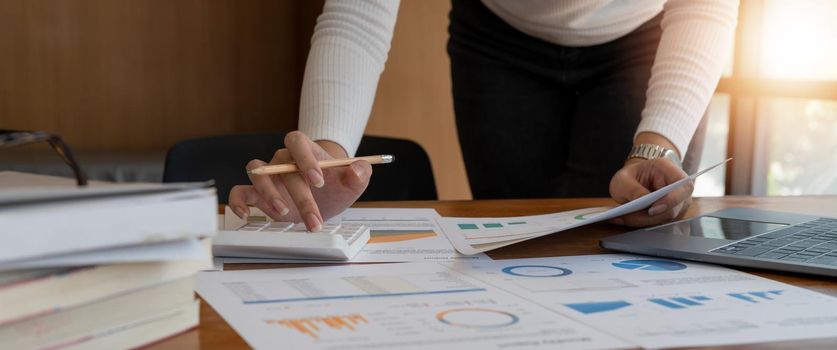 Close up of businesswoman or accountant working on calculator to calculate business financial data, accountancy document and laptop computer at office, business concept.