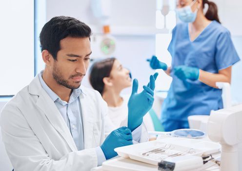 Shot of a dentist applying his gloves while selecting the tool he needs.