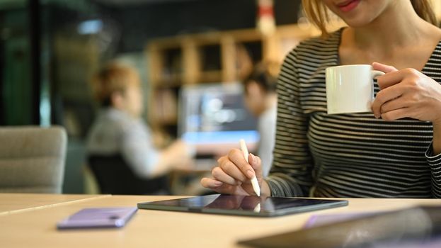 Cropped shot young female team leader using digital tablet while sitting in software company office.