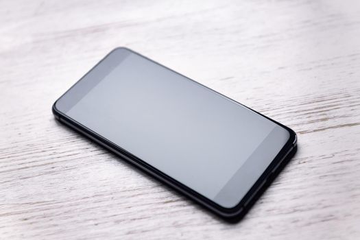 top view of a smart phone with blank screen on white wooden table, technology and communication concept, copy space for text, selective focus