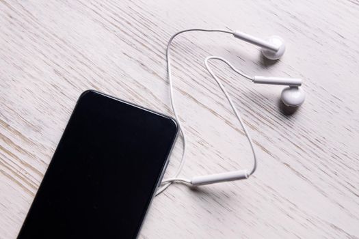 top view of a smart phone with earphones on white wooden table, music and podcast concept, copy space for text