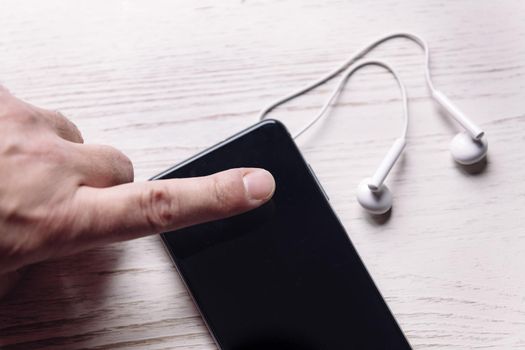 top view of a finger touching a smartphone with earphones on white wooden surface, music and podcast concept, copy space for text