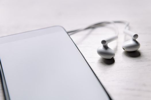 smart phone with earphones on white wooden table, music and podcast concept, copy space for text