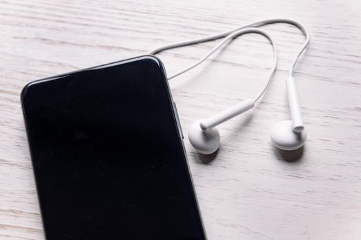 top view of a smartphone with earphones on white wooden surface, music and podcast concept, copy space for text