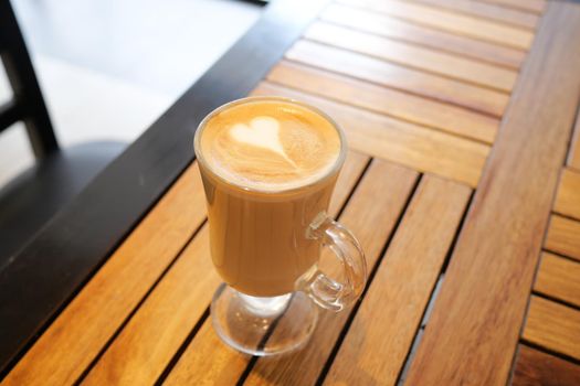 a cup of late coffee with flower shape design on top at cafe .