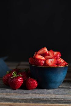 Fresh sliced strawberries in bowl with whole strawberries beside them, low key lighting and vertical orientation.