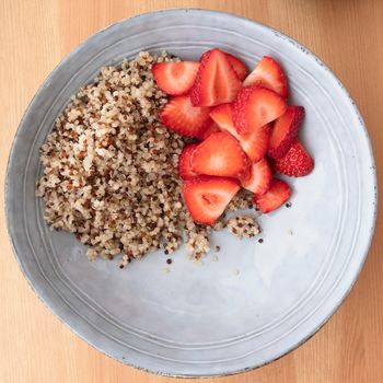 Blue bowl with quinoa and strawberry slices on wooden surface, image 3 of 8