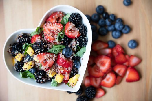 Healthy quinoa fruit salad in heart shaped bowl, flat lay.
