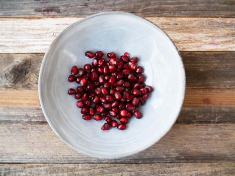 Fresh pomegranate seeds in bowl on wooden surface, flat lay.