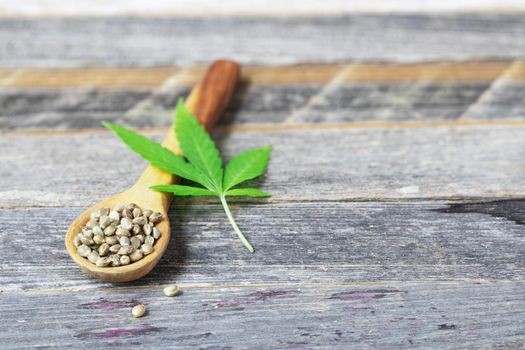 Cannabis seeds in a wooden spoon with leaf on a wooden surface with copy space.