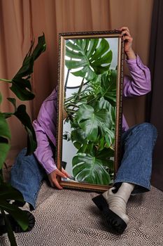 Jungles in the mirror. Woman holds mirror reflecting home jungles with Monstera plant.