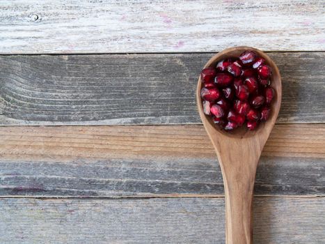 Pomegranate seeds in a wooden spoon on rustic wooden surface with copy space.