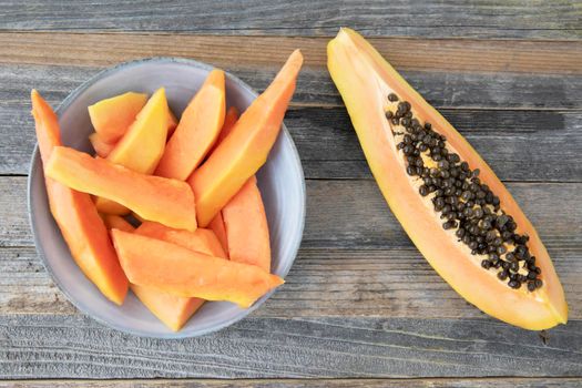 Quarter slice of a papaya on a wooden surface and a blue bowl and peices of cut payapa.