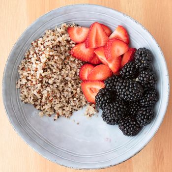 Blue bowl with quinoa, strawberry slices and blackberries on wooden surface, image 4 of 8