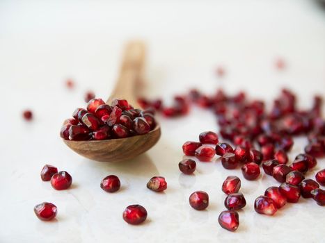 Pomegranate seeds in a wooden spoon and on a marble surface