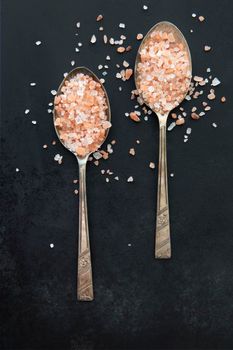 Pink Himalayan salt in old spoons on black background.