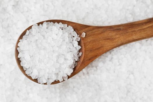 Salt crystals in wooden spoon on bed of salt.