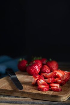Sliced and whole strawberries on cutting board with knife, low key lighitng and vertical orientation.