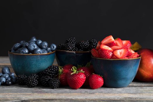 Fresh strawberreis, blueberries and blackberries in blue bowls surrounded by fruit.