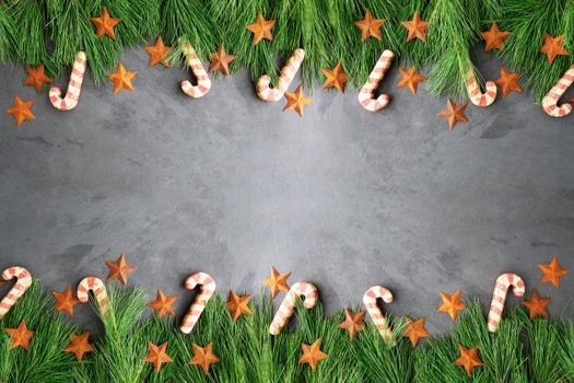 Christmas border of pine boughs, rustic stars and wooden candy canes on slate surface, copy space in the middle.