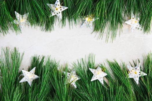 Pine boughs and star lights on marble surface with copy space in the middle.