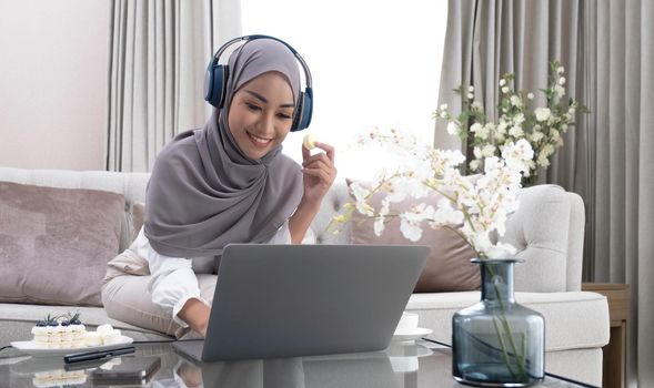 Happy Arab housewife in hijab relaxing with sweets and coffee on sofa at home enjoy indoor relaxation Relax on the comfy sofas, free space..