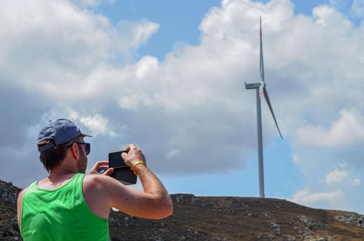 man capture on smartphone a wind turbine on the mountain with clouds on background