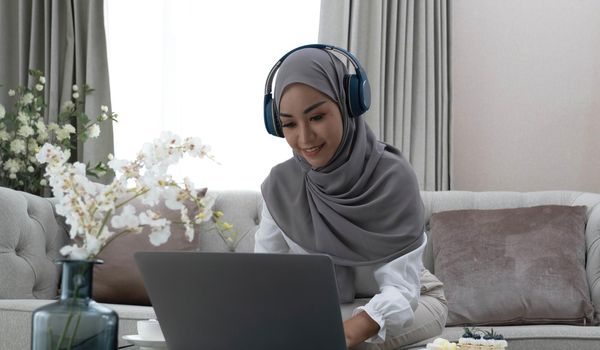 Online Tutoring. Young muslim woman teacher having video call with students, talking at laptop camera, sitting on couch at home.