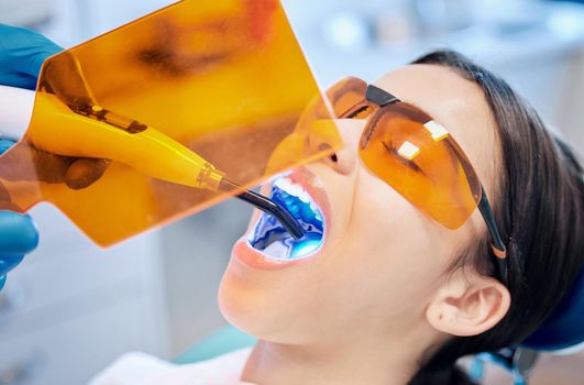 Shot of a young woman getting her teeth whitened by her dentist.