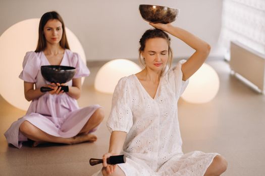 Two female yoga teachers playing a Tibetan bowl in the gym during a yoga retreat.