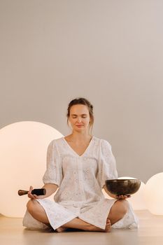 Portrait of a female yoga teacher playing a Tibetan bowl or singing a bell in the gym during a yoga retreat.